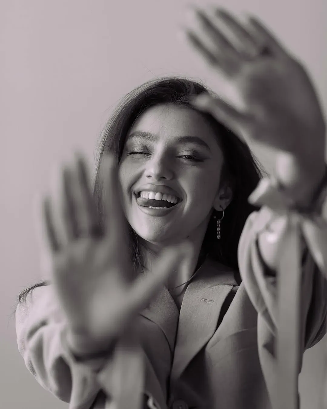 Black and white portrait of a woman laughing with her eyes closed, both hands raised blurred toward the camera.